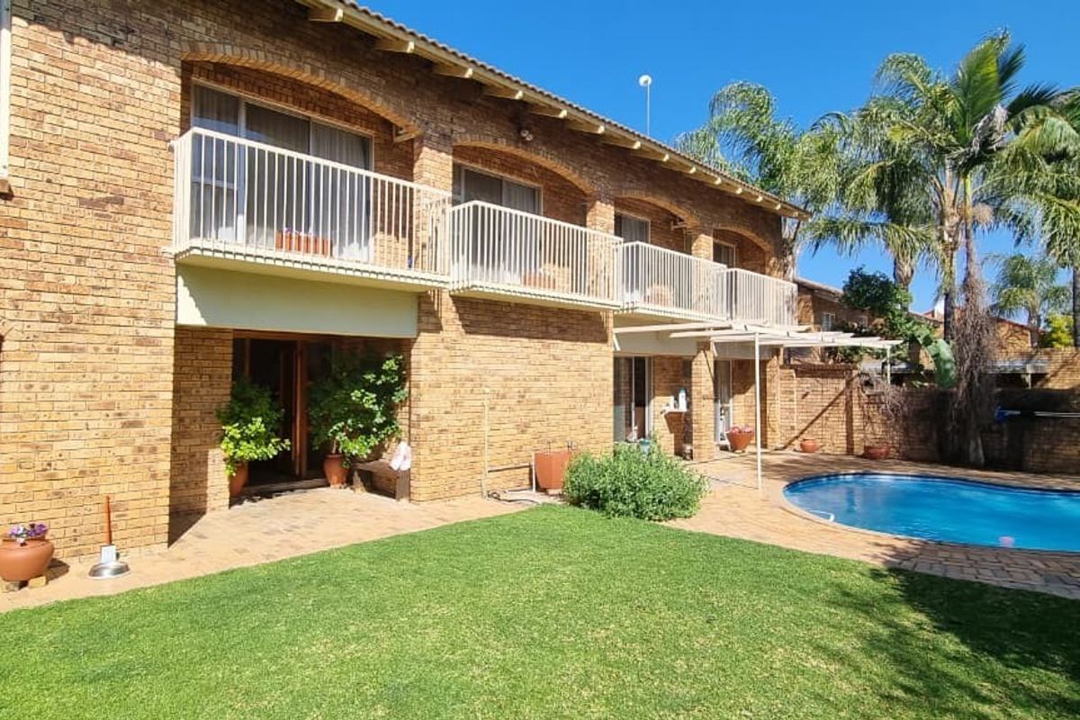 Rear view of a double-story brick house featuring a swimming pool, paved patio area, and upper-level balconies with metal railings.