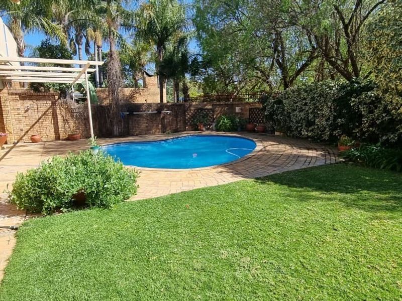 A private backyard featuring a swimming pool, paved patio area, established garden, and a brick-walled perimeter.