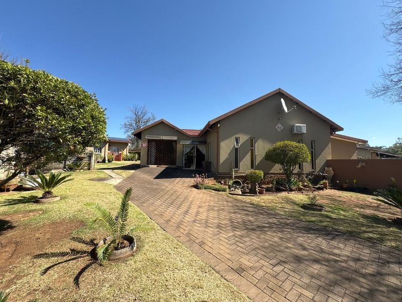 Front view of a single-story house featuring a paved driveway, landscaped garden, tiled roof, and exterior air conditioning unit.