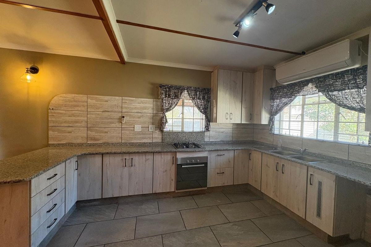 A spacious kitchen featuring light wood-look cabinetry, granite countertops, a built-in oven with gas hob, and tiled flooring.