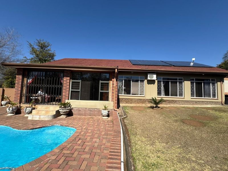 Rear view of the property featuring a swimming pool, brick paved patio, solar panels on the roof, and an outdoor air conditioning unit.