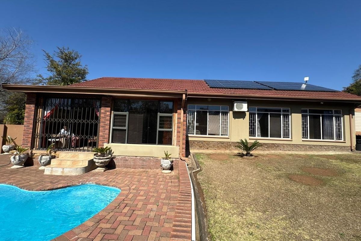 Rear view of the property featuring a swimming pool, brick paved patio, solar panels on the roof, and an outdoor air conditioning unit.