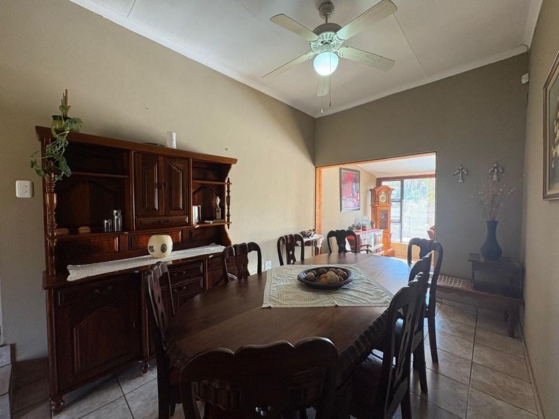 A traditional dining room featuring tiled flooring, a ceiling fan, and coved cornicing, with an open transition to an adjacent living space.