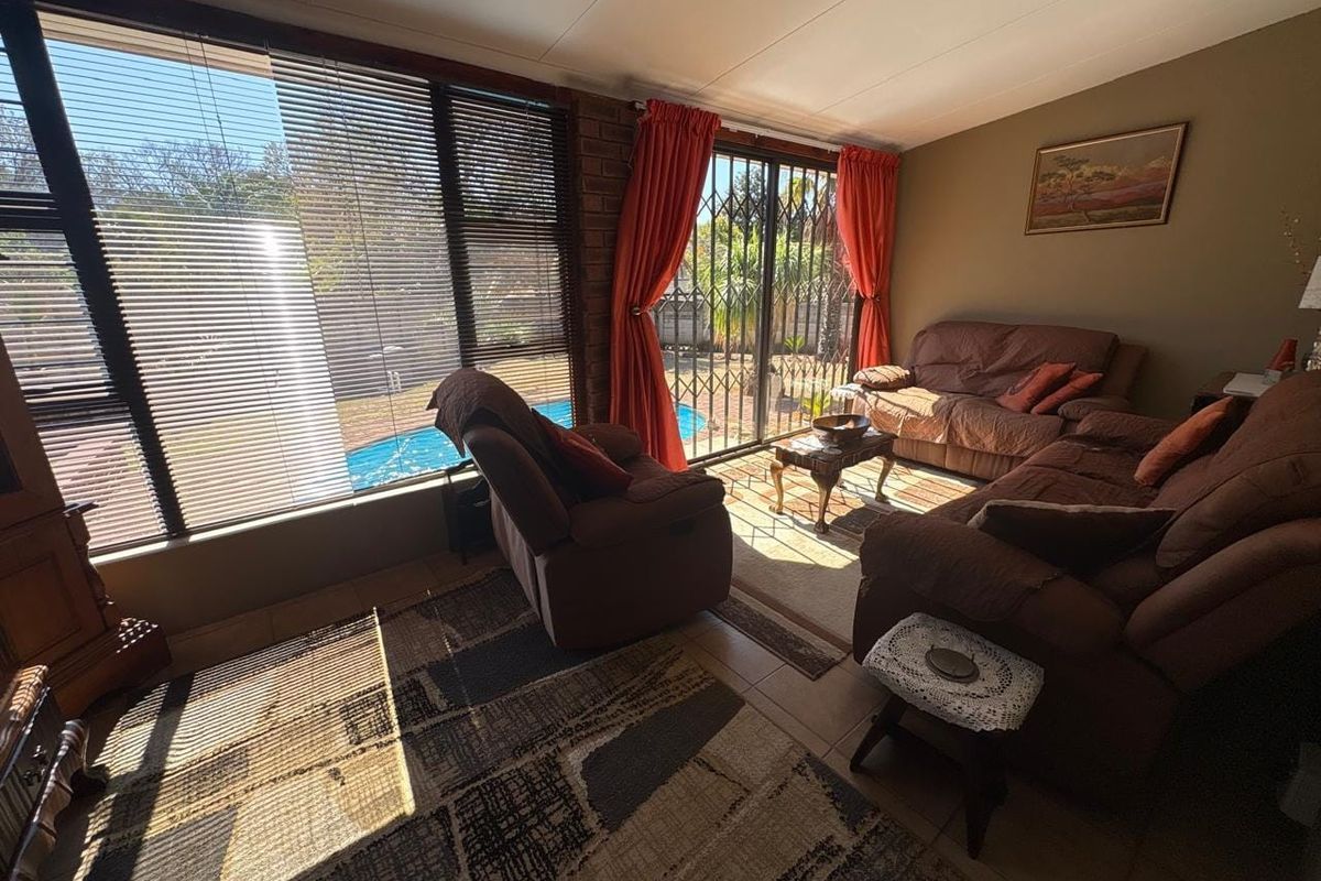 A sunlit living room featuring tiled floors, an exposed brick feature wall, and large sliding glass doors providing direct access to the pool area.