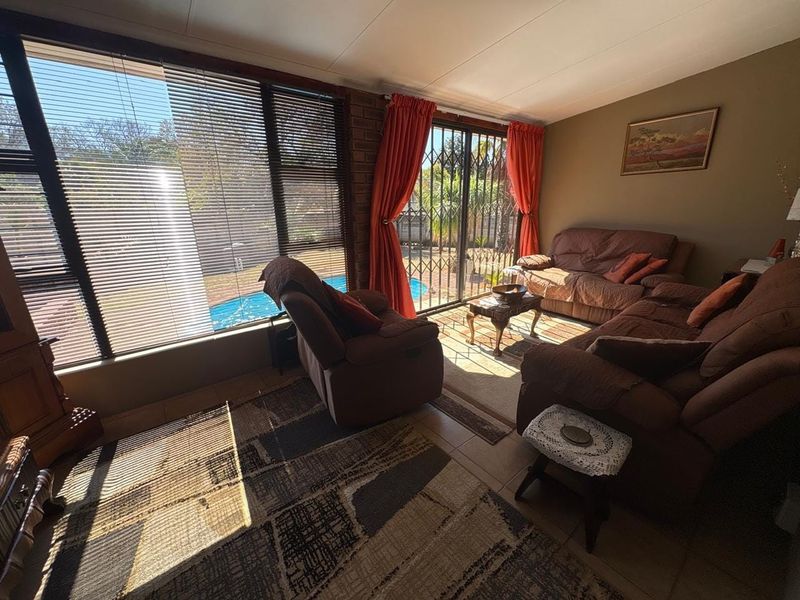 A sunlit living room featuring tiled floors, an exposed brick feature wall, and large sliding glass doors providing direct access to the pool area.