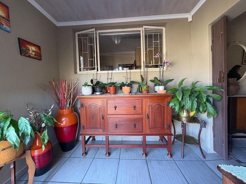 A covered patio area featuring tiled flooring and a window with security bars, providing a view into the interior of the home.