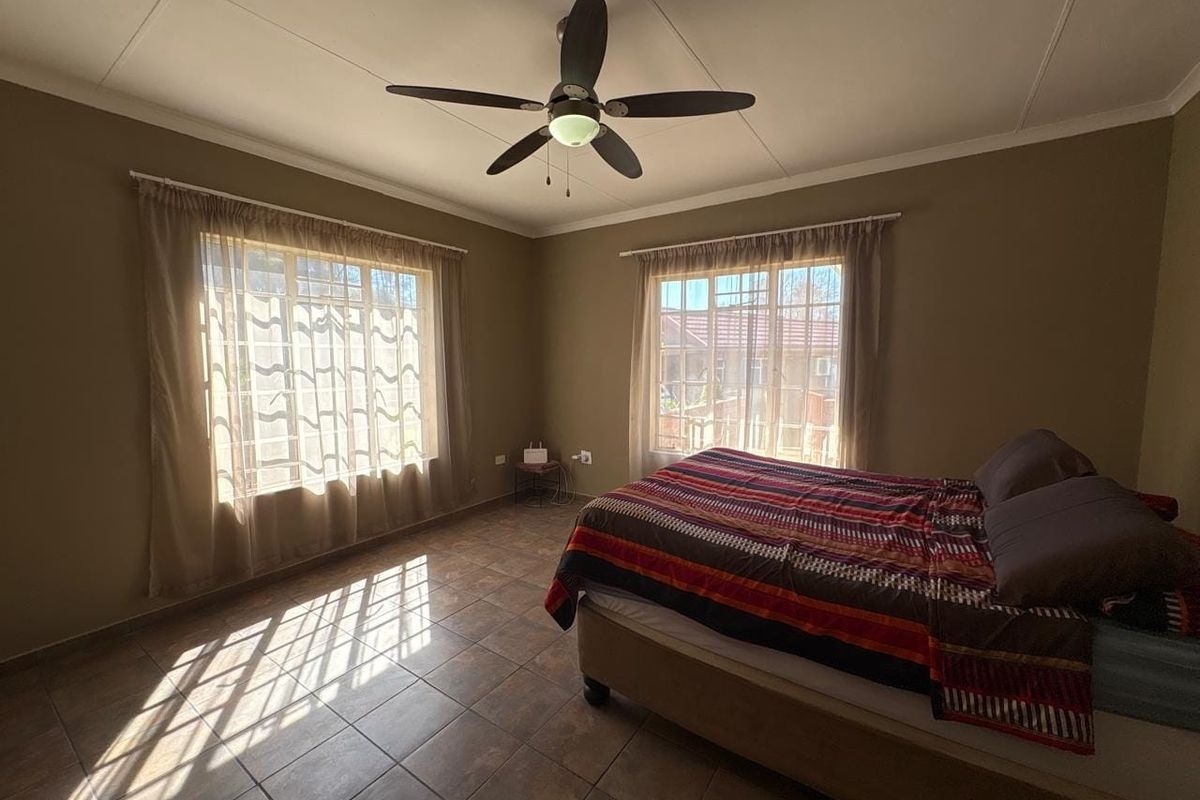 A spacious bedroom featuring tiled flooring, a ceiling fan, and large windows that provide ample natural light.