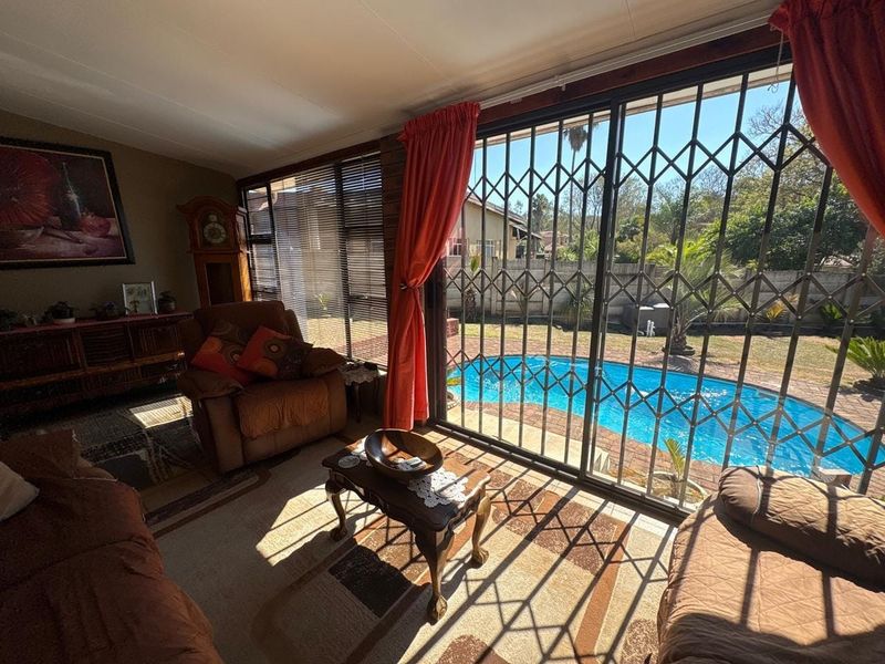 A living room featuring large sliding glass doors with security gates, providing direct access and views to the outdoor swimming pool area.