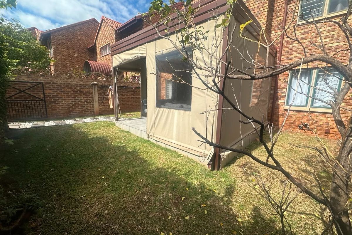 Rear garden area featuring a brick townhouse facade, a lawn, and an enclosed patio structure with canvas and vinyl screening.