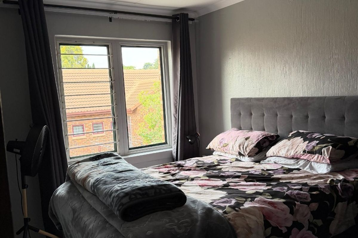 A functional bedroom featuring tiled flooring, a window with security bars, and a central ceiling light fixture.