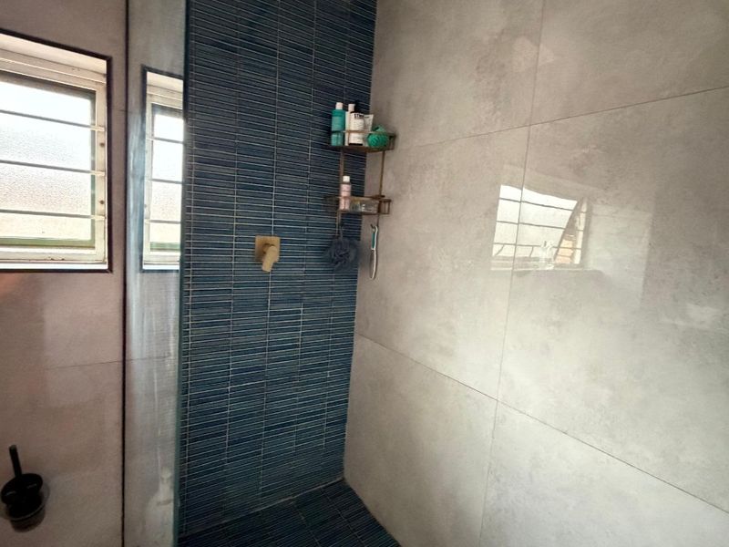 Modern walk-in shower featuring blue mosaic accent tiling, a large rain shower head, and a frameless glass screen in a contemporary bathroom.