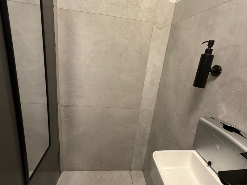 A modern, compact bathroom featuring neutral large-format wall and floor tiles, a wall-mounted basin, and a sleek mirror.