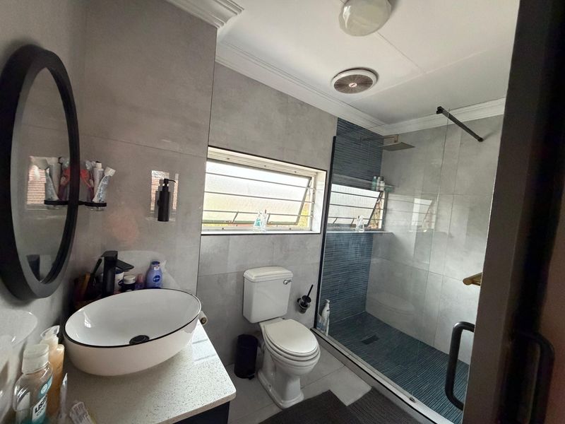 Modern bathroom featuring a vessel sink on a stone vanity, a spacious walk-in shower with a rain shower head, and contemporary grey tiling.