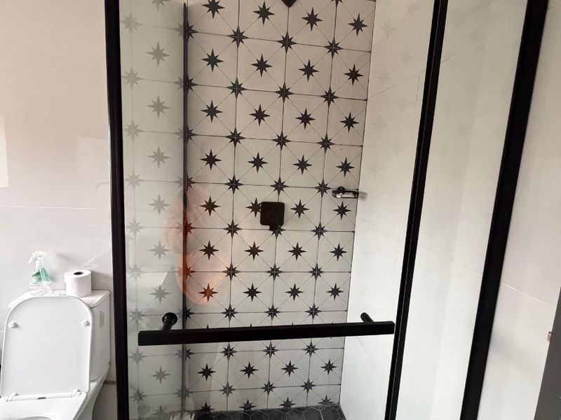 Modern bathroom featuring a walk-in shower with black framed glass screen, patterned wall tiles, and hexagonal floor tiling.