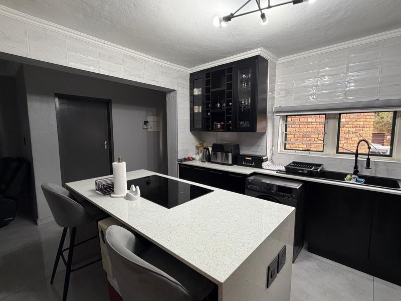 Modern kitchen featuring a central island with an induction hob, sleek black cabinetry, quartz countertops, and a stylish subway tile backsplash.