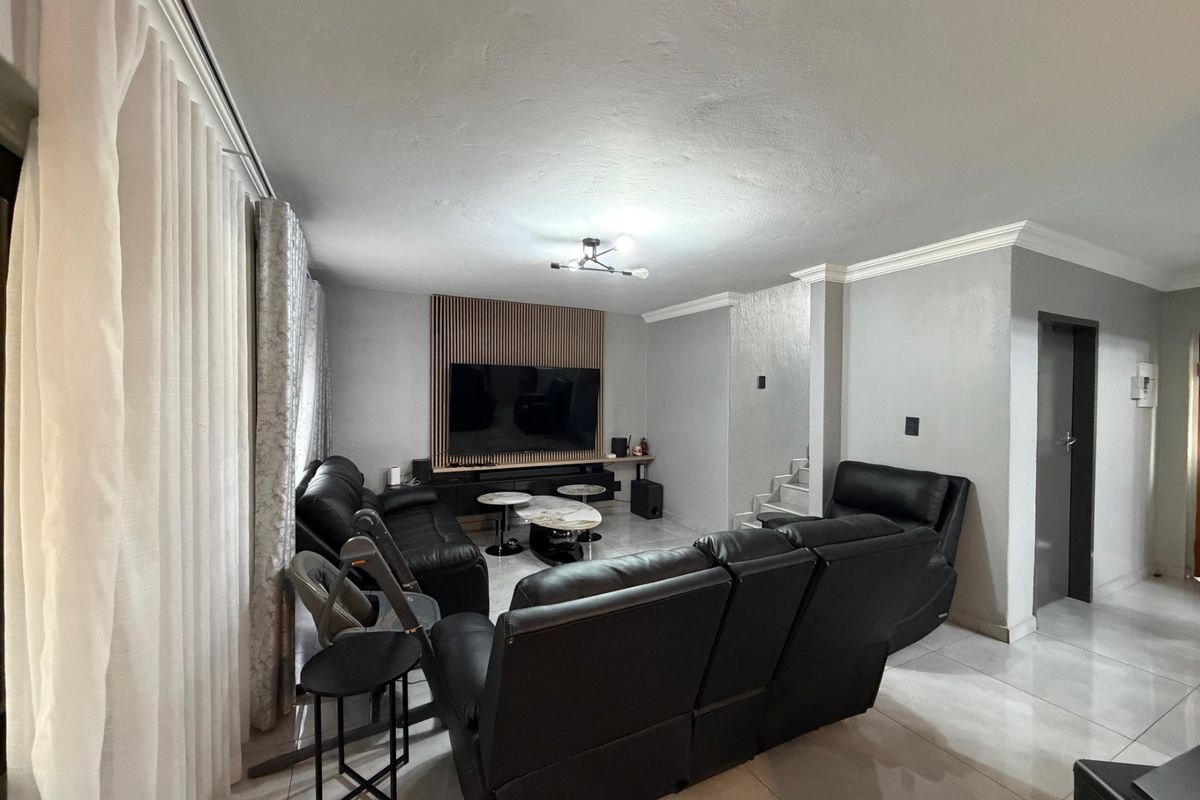 Spacious living room featuring tiled flooring, a modern slatted wood feature wall, and crown molding, providing a contemporary and well-maintained living space.