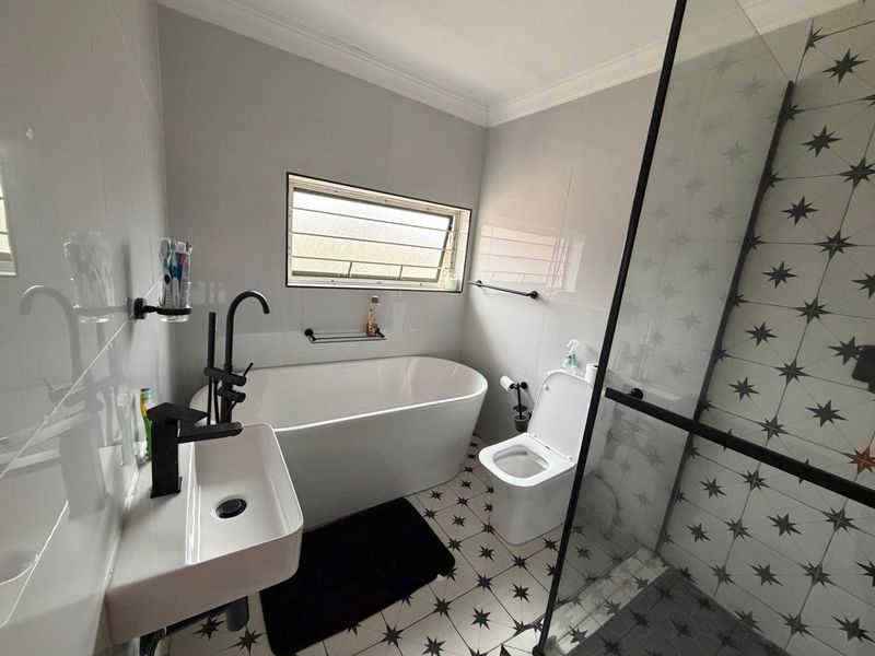 Modern bathroom featuring a freestanding bathtub, walk-in shower with glass enclosure, wall-mounted basin, and stylish patterned floor tiles.
