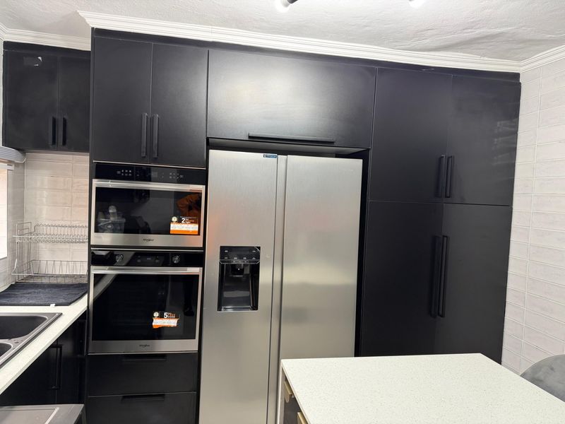 Modern kitchen featuring sleek black cabinetry, integrated stainless steel appliances, built-in oven and microwave, and a stone countertop.