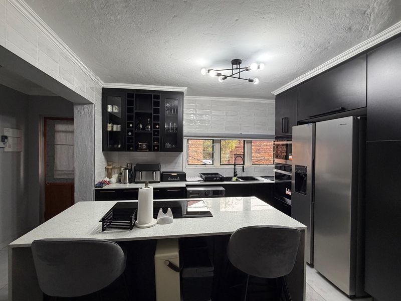 Modern kitchen featuring sleek black cabinetry, a central island with quartz countertops, integrated appliances, and a stylish tiled backsplash.