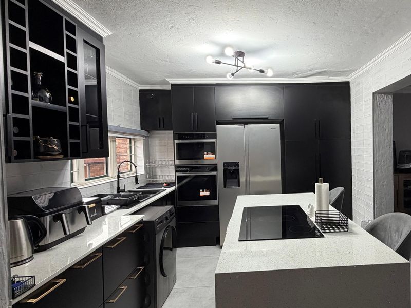 Modern kitchen featuring matte black cabinetry, quartz countertops, a central island with an induction cooktop, and integrated built-in appliances.