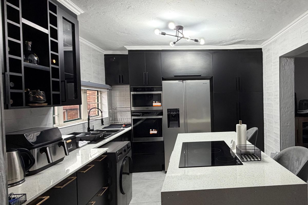 Modern kitchen featuring matte black cabinetry, quartz countertops, a central island with an induction cooktop, and integrated built-in appliances.