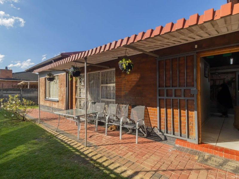 A covered brick patio area featuring a metal awning and security gate, providing direct access to the home and overlooking the garden.