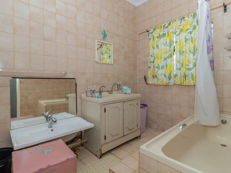 A dated bathroom featuring a built-in bathtub, wall-mounted basin, and vanity cabinet with full-height ceramic wall tiling.