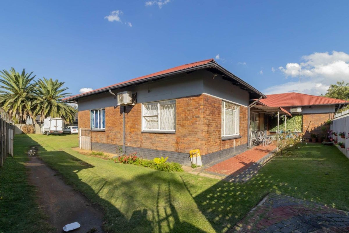 Rear view of the property featuring a brick facade, corrugated metal roof, and a well-maintained garden area with a paved walkway.