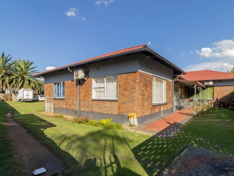 Rear view of the property featuring a brick facade, corrugated metal roof, and a well-maintained garden area with a paved walkway.