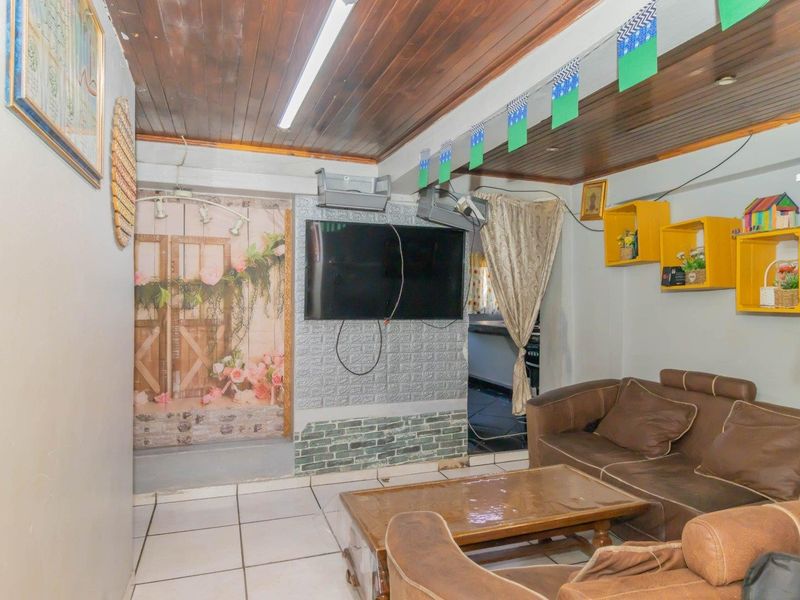 A living room featuring a timber-clad ceiling, tiled flooring, and a faux-brick accent wall, offering a dated aesthetic with potential for modernization.