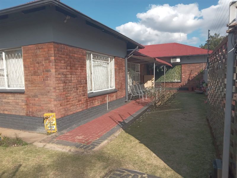 Rear view of the property featuring a brick facade, paved walkway, lawn, and secure boundary walling.