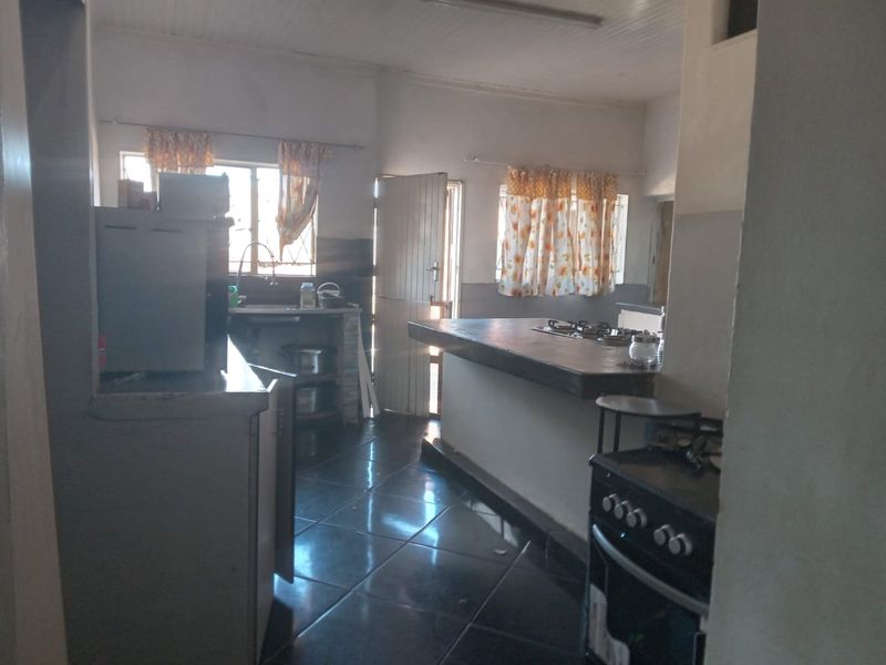A functional kitchen featuring a central island with a gas hob, tiled flooring, and a timber ceiling, offering potential for modernization.