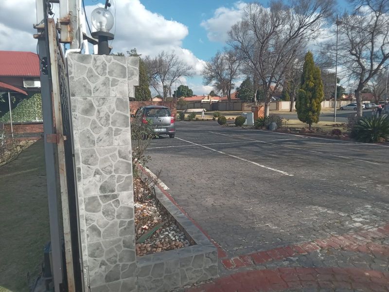 Front exterior view showing a paved driveway, stone-clad gate pillar, and boundary wall leading to the property entrance.