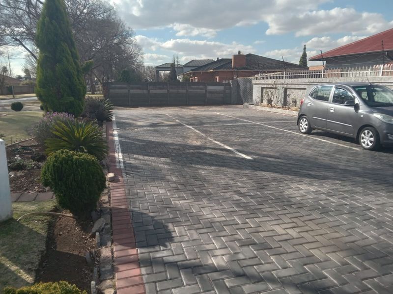 A paved driveway area featuring marked parking bays, perimeter walling with electric fencing, and established garden landscaping.