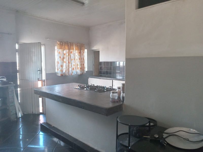 A functional kitchen featuring a central island with a built-in gas hob, tiled backsplash, and tiled flooring, offering a practical layout for daily cooking.