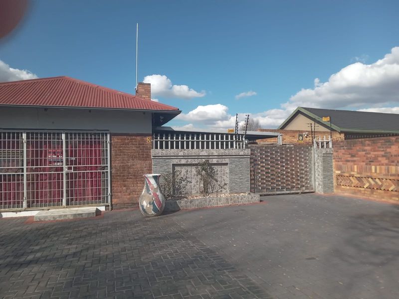 Front exterior view of the property featuring a brick facade, metal roof, paved driveway, and secure boundary wall with electric fencing.