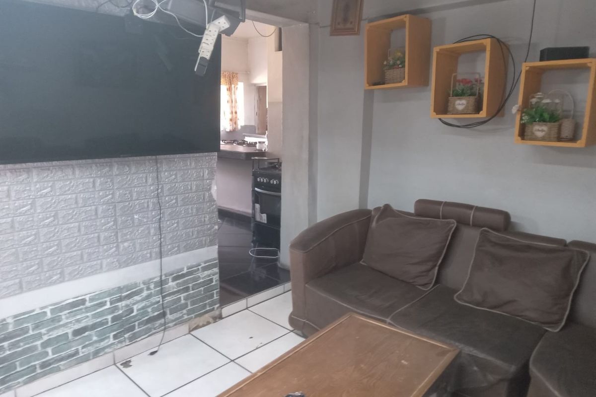 Living room area featuring ceramic floor tiles and faux brick wall cladding, with an adjacent view into the kitchen space.