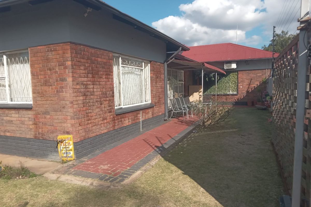 Rear view of the property featuring a brick facade, paved walkway, and a secure boundary wall with a well-maintained lawn area.