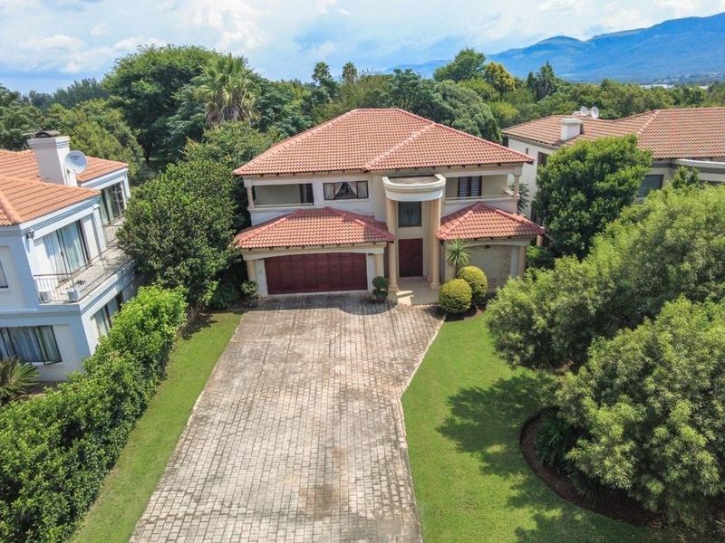 Aerial view of a two-story residential property featuring a tiled roof, paved driveway, double garage, and established garden surroundings.