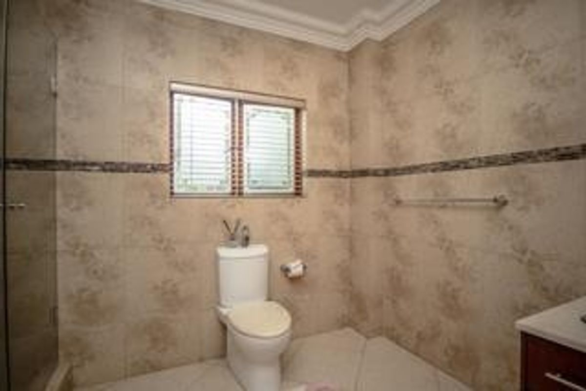 A functional bathroom featuring tiled walls and flooring, a shower enclosure, a toilet, and a vanity cabinet with a towel rail.