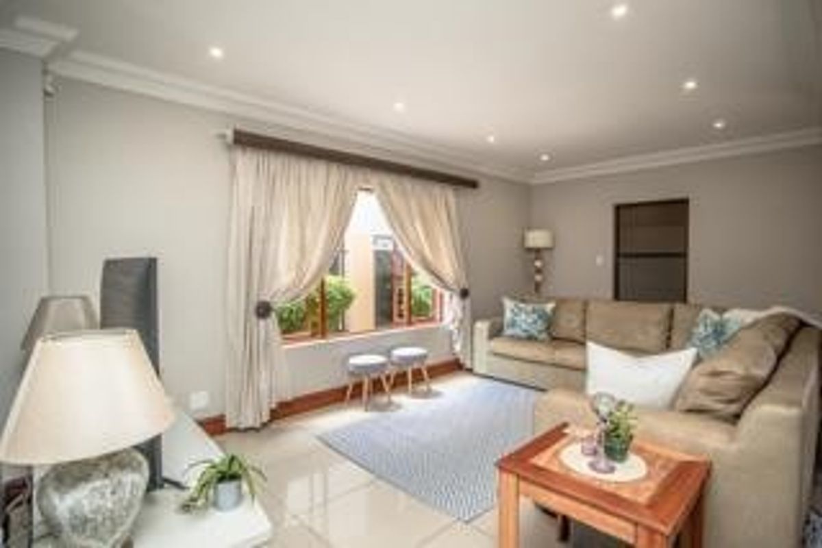 A well-maintained living room featuring neutral walls, tiled flooring, recessed downlighting, and large windows with curtains.