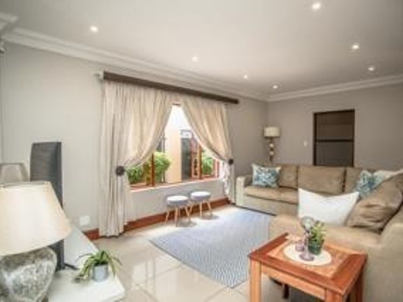 A well-maintained living room featuring neutral walls, tiled flooring, recessed downlighting, and large windows with curtains.