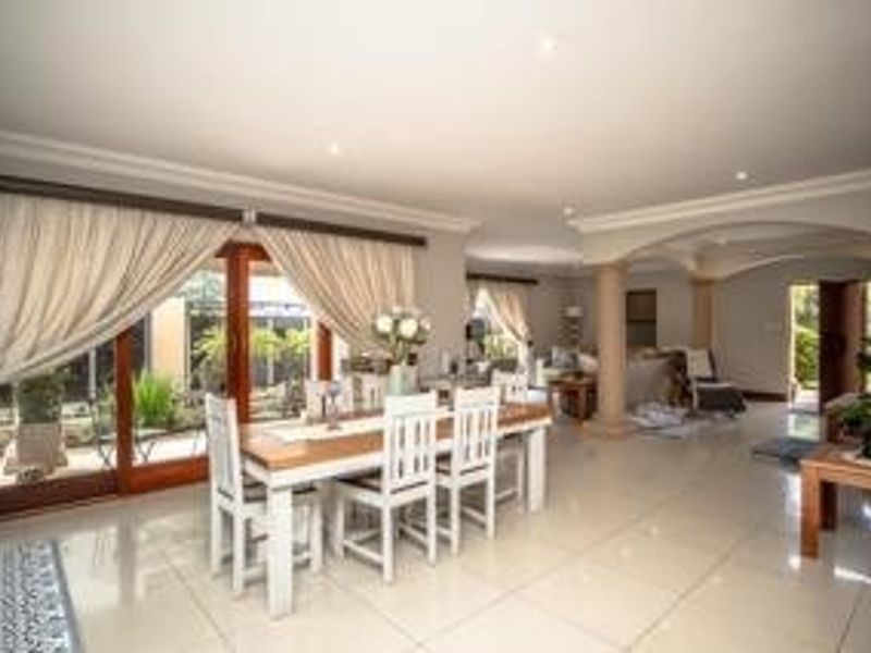 Spacious open-plan living and dining area featuring large sliding glass doors, tiled flooring, and elegant architectural columns connecting to adjacent living spaces.