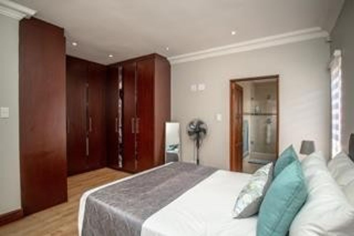A well-maintained bedroom featuring dark wood built-in cupboards, laminate flooring, and direct access to an en-suite bathroom.