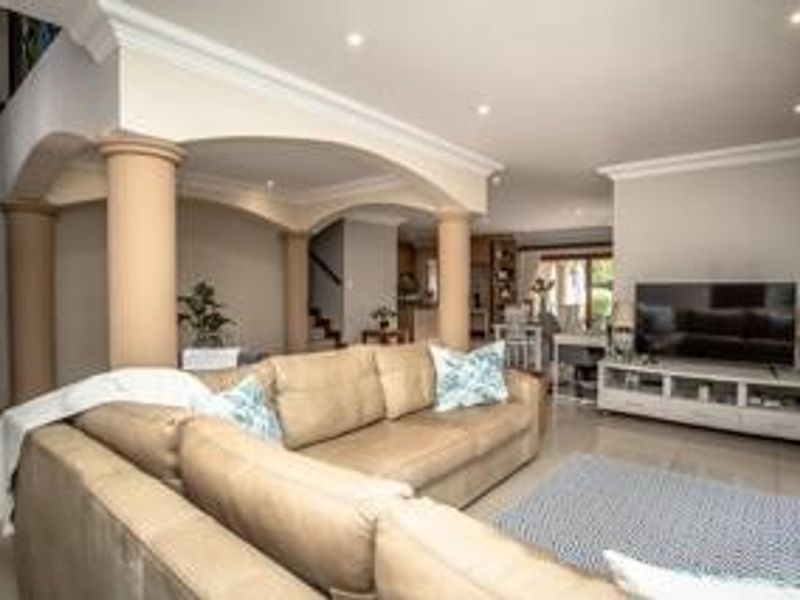 Spacious open-plan living area featuring elegant arched architectural columns, recessed downlighting, and neutral tiled flooring, creating a bright and inviting atmosphere.