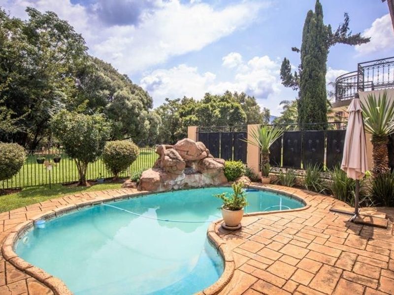 A private outdoor pool area featuring a decorative rock water feature, paved surround, and secure perimeter fencing set within a landscaped garden.
