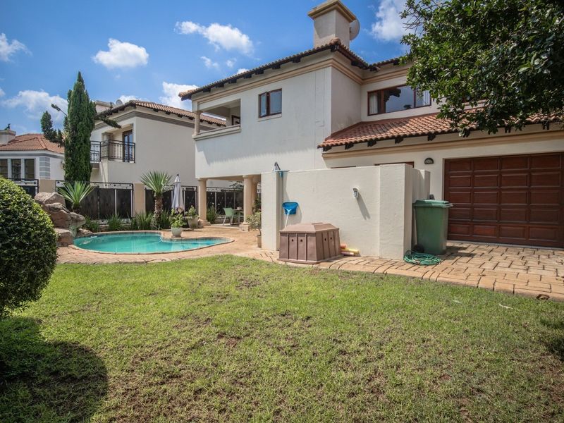 Rear view of the property featuring a private swimming pool, paved patio area, landscaped lawn, and access to the garage.