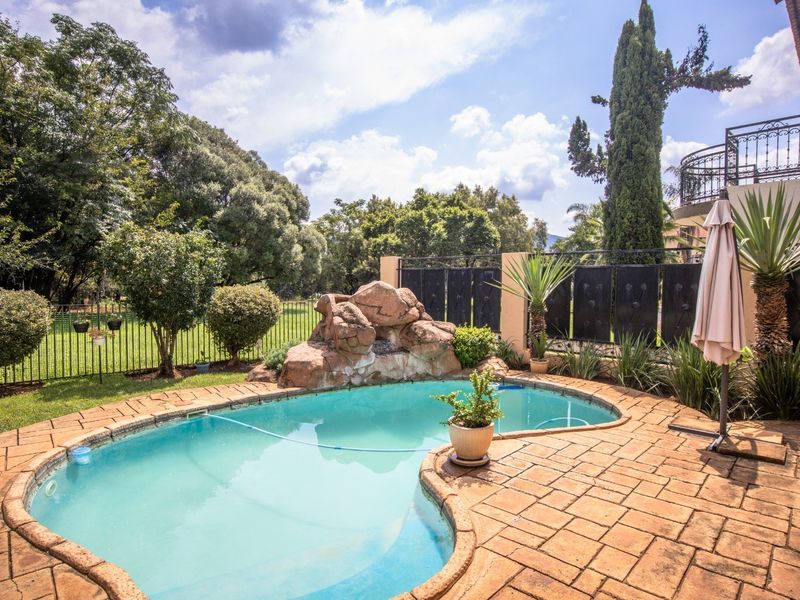 Outdoor pool area featuring a kidney-shaped swimming pool with a built-in rock water feature and surrounding paved patio space.