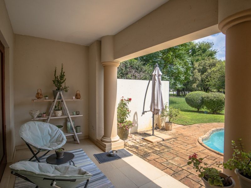 A covered patio area featuring tiled flooring and structural columns, overlooking a private garden and swimming pool.