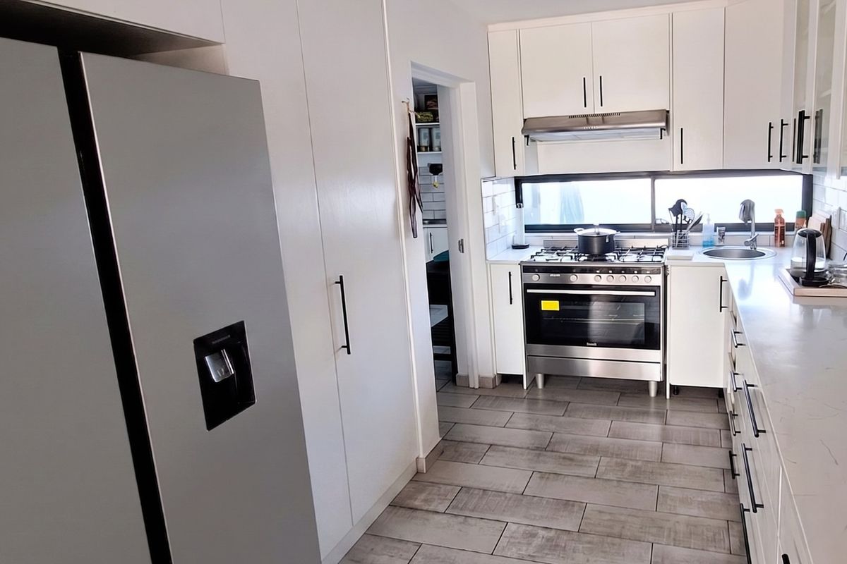 Modern kitchen featuring white cabinetry, stone countertops, gas stove with extractor fan, and tiled flooring, with an adjacent scullery area.